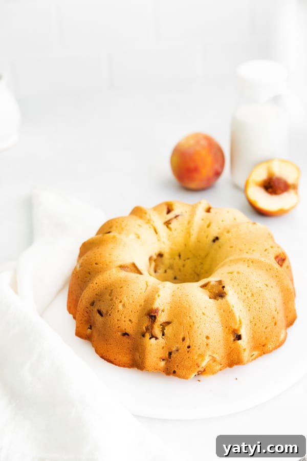 Glazed Peach Bundt Cake Recipe with Fresh Summer Peaches 3 Peach Bundt Cake on a cake plate with some fresh peaches in the background.