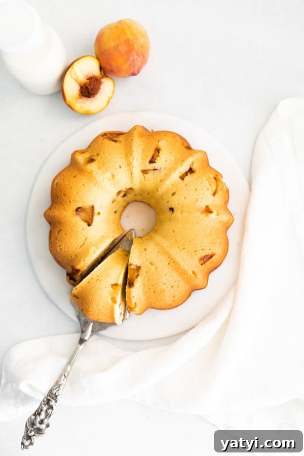 Glazed Peach Bundt Cake Recipe with Fresh Summer Peaches 5 Peach Bundt Cake on a serving platter with a sliced pieces on a server knife.