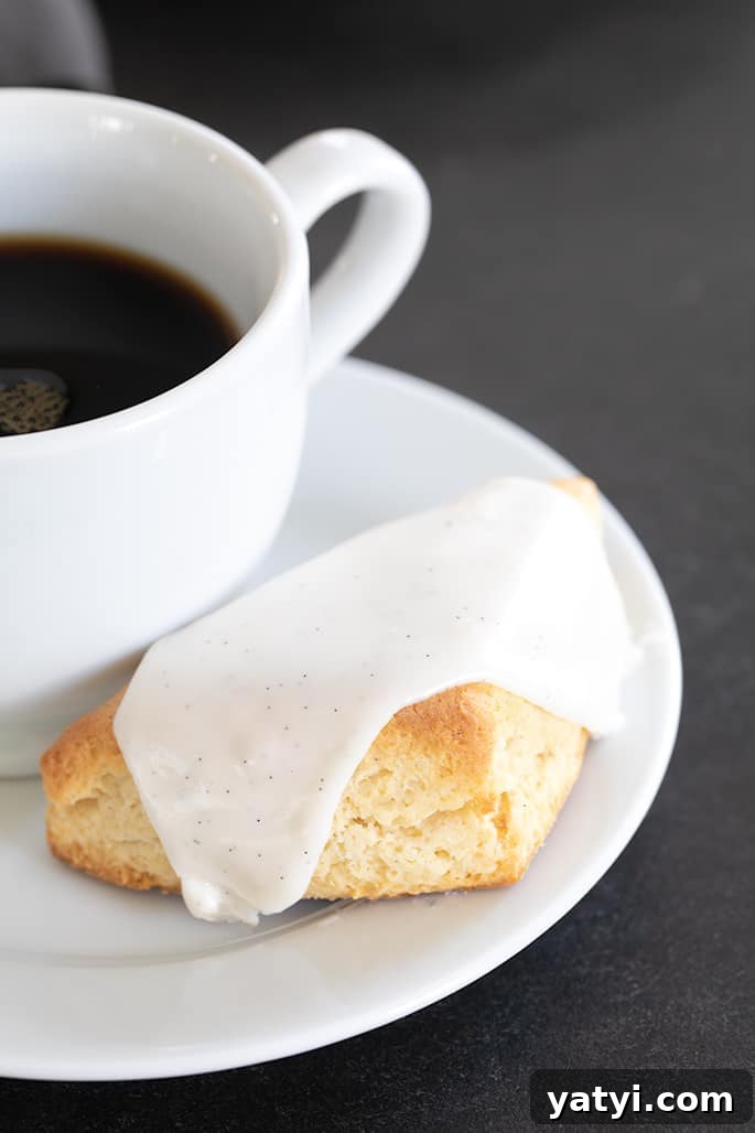Gluten-Free Vanilla Scones Inspired by Starbucks 5 A close up of a vanilla scone with white icing and coffee on a small plate