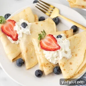 Crepes on a white plate topped with fresh blueberries, strawberries and whipped cream