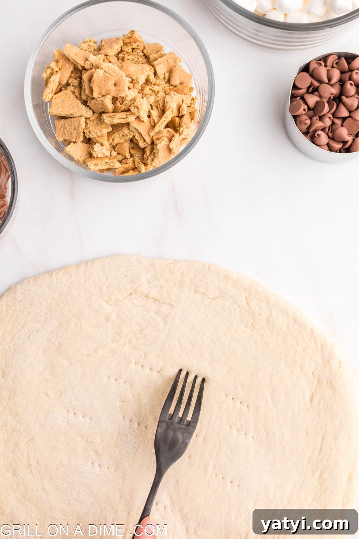 Crushed graham crackers in a bowl with the dough rolled out and a fork poking holes