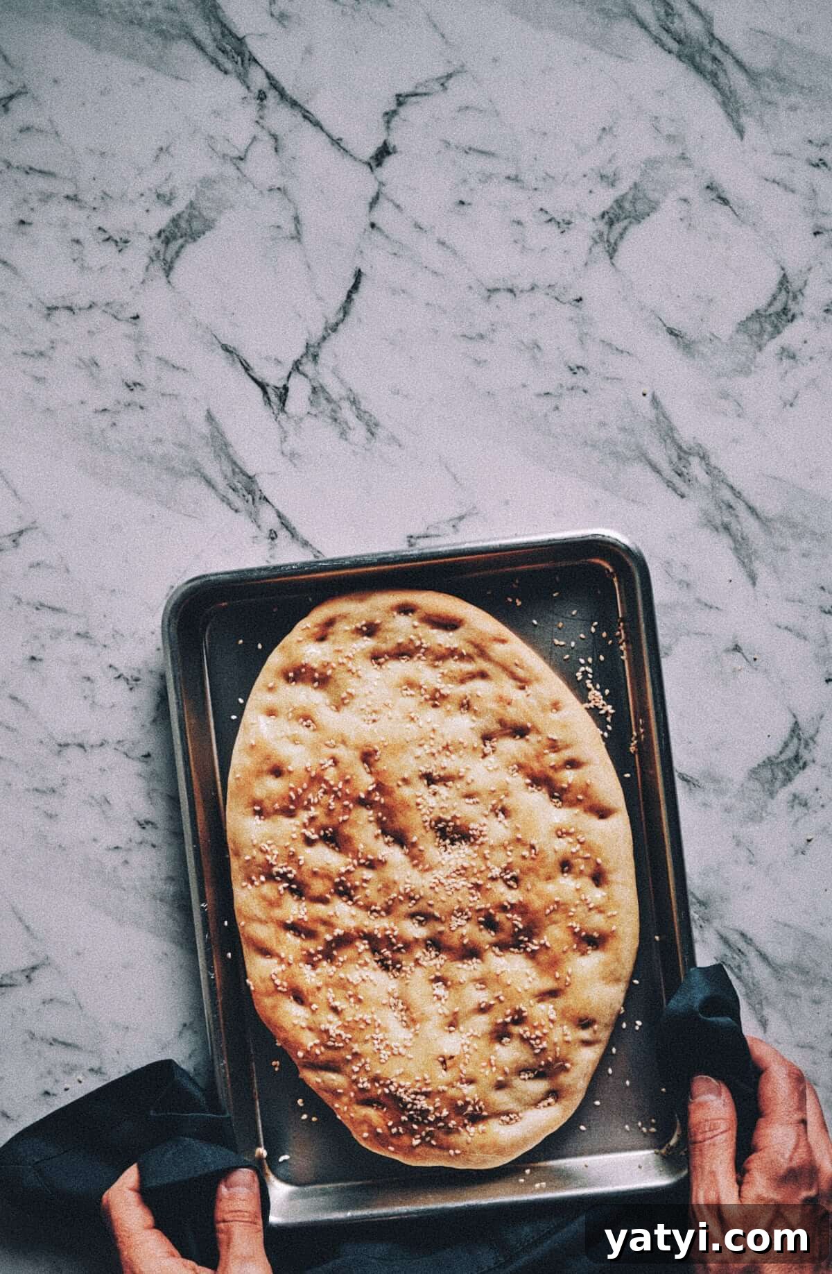 Greek Easter Traditions: Customs, Foods, and Celebrations Explained 3 freshly baked bread on a baking tray being handled by two hands with a kitchen towel