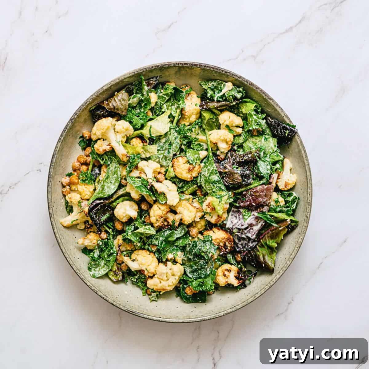 a bowl of roasted cauliflower salad on a white marble table.