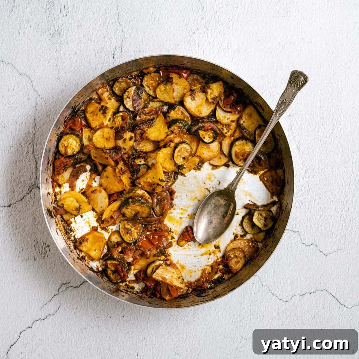 a round baking dish filled with roasted vegetables with a serving spoon.