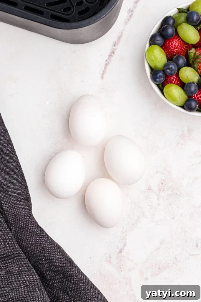 Perfect Soft-Boiled Eggs in an Air Fryer 3 Four eggs on a marble table in front of an air fryer basket and a bowl of fruit.