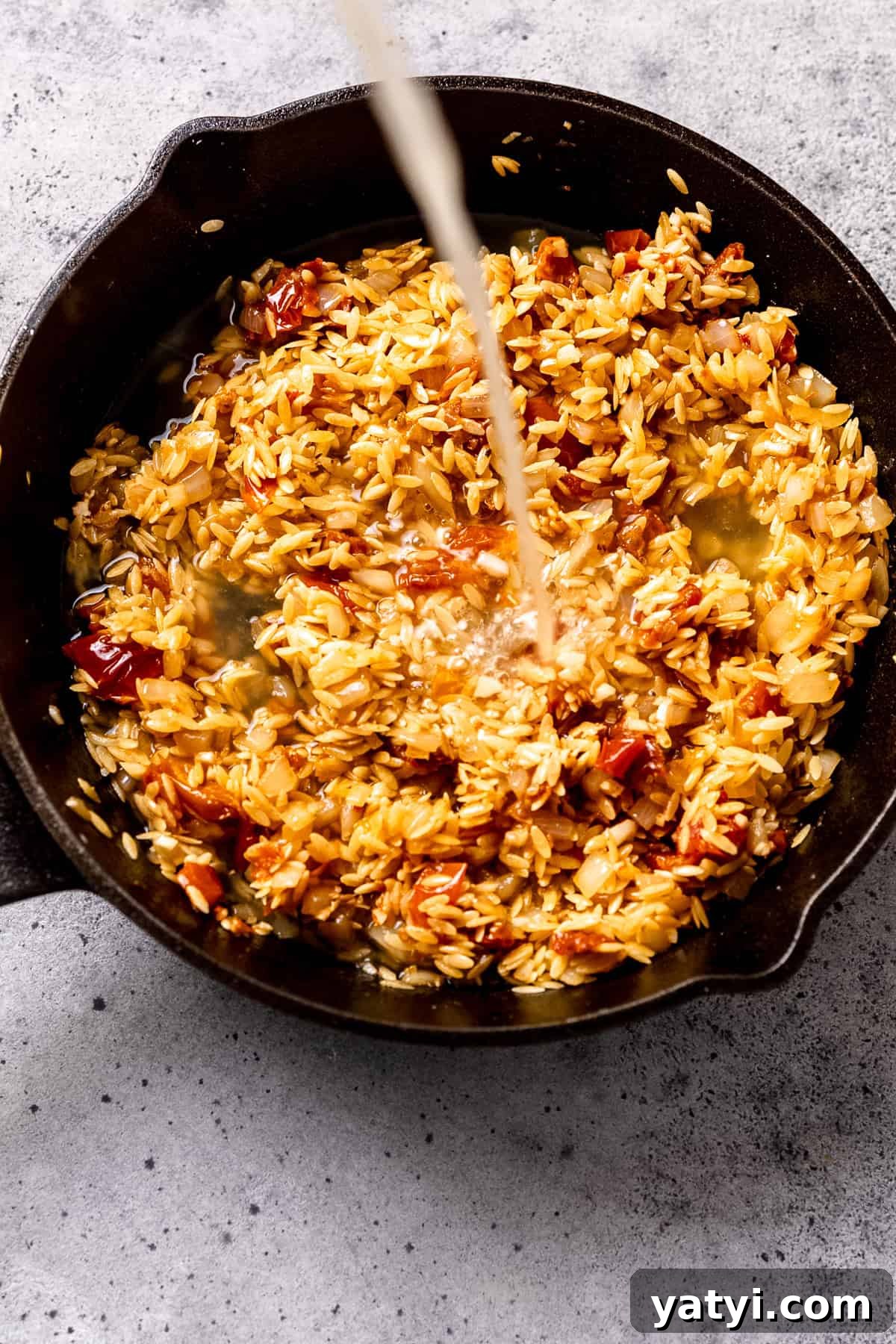 Tuscan Chicken Orzo with Sun-Dried Tomatoes and Spinach 7 Stock or broth being mixed into the orzo to cook it all in one pot.