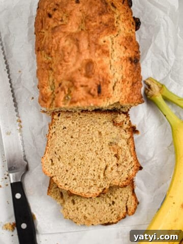 The slices of sourdough discard banana bread are shown with bananas on the right side and a serrated knife on the left side of the loaf.