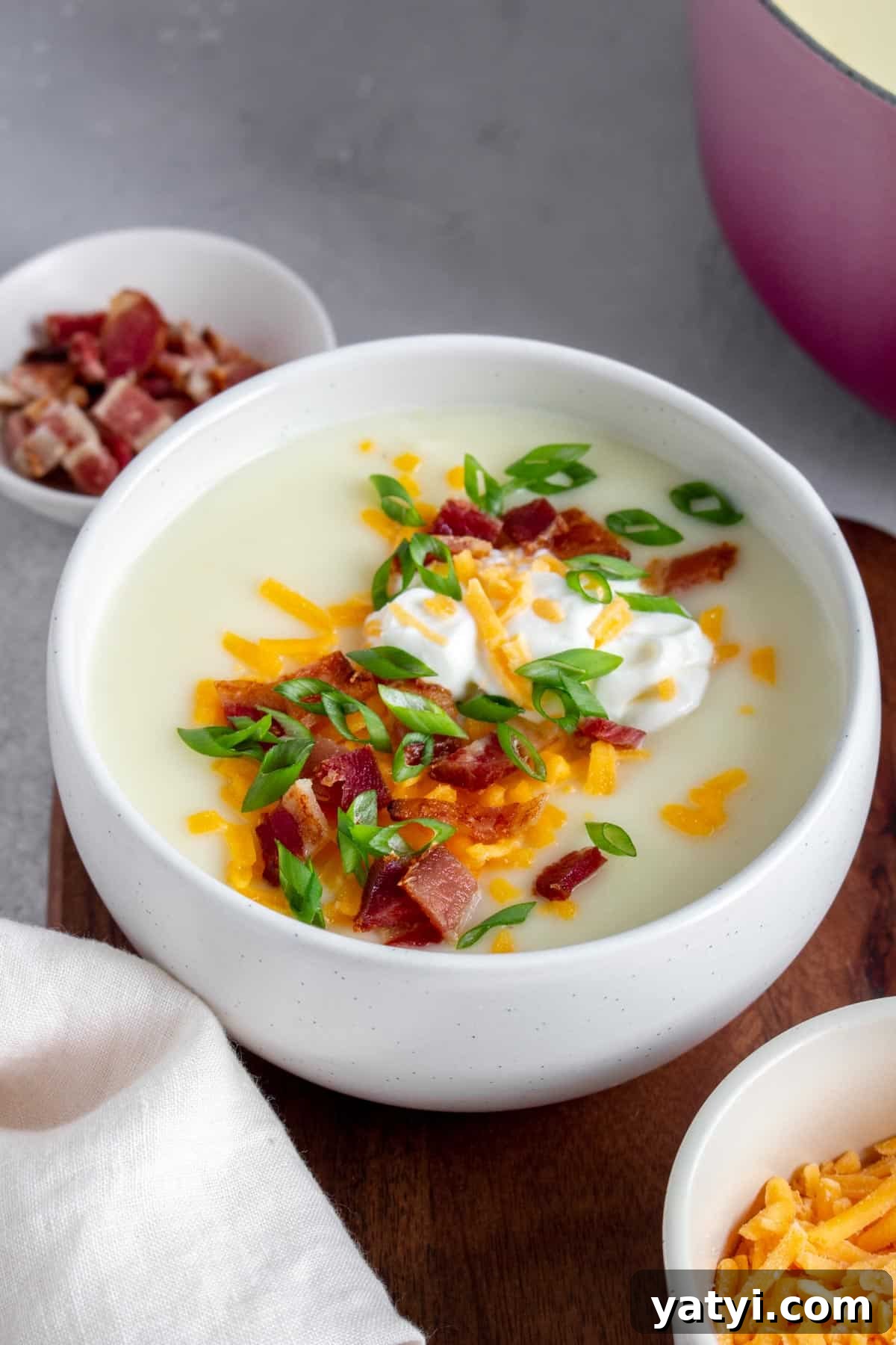Creamy 4-Ingredient Potato Soup Recipe 7 A bowl of potato soup with sour cream, shredded cheese, bacon, and green onions.