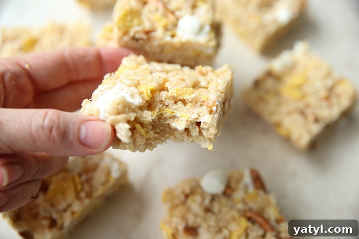 A cut sweet and salty rice crispy treat with a bite out of a corner held above more sliced rice crispy treats.