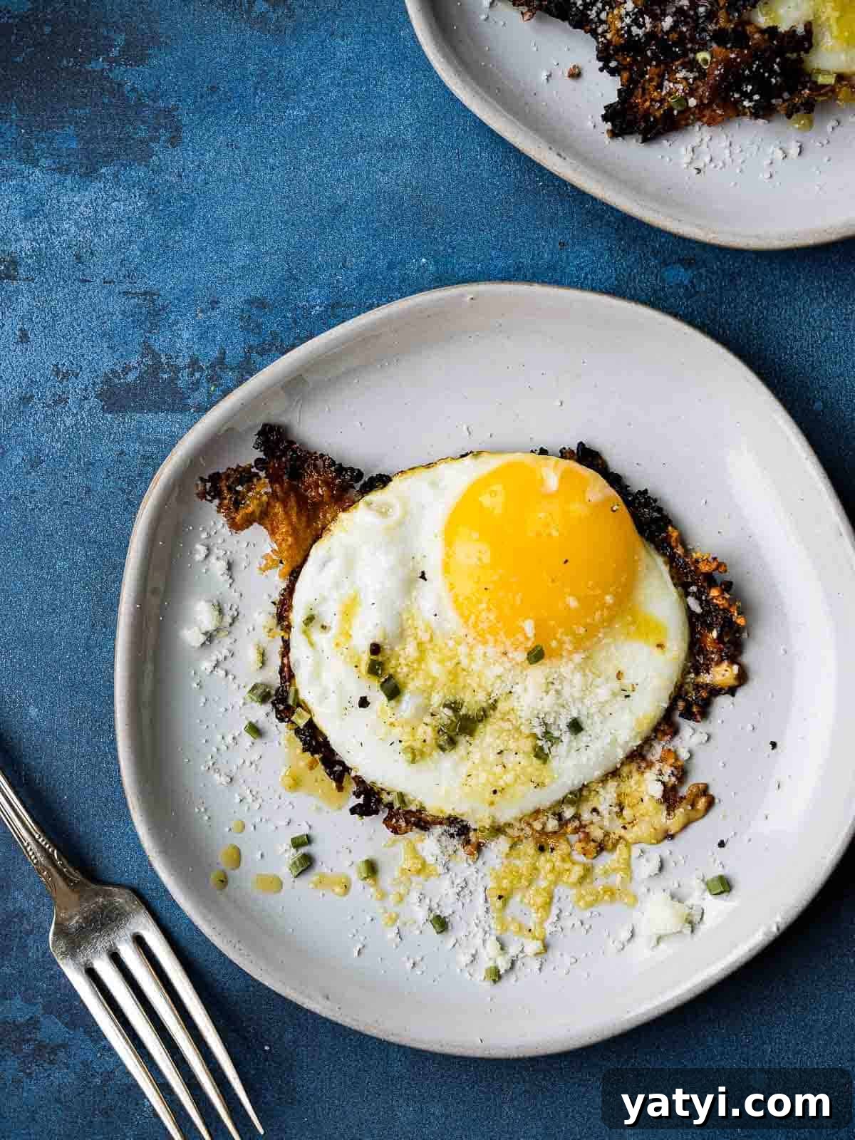 Overhead picture of a fried egg on a white plate, on top of a blue background.