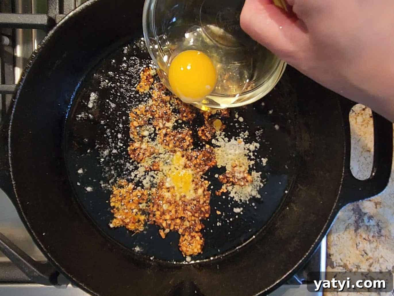 An egg is poured into a hot skillet for frying with spices.