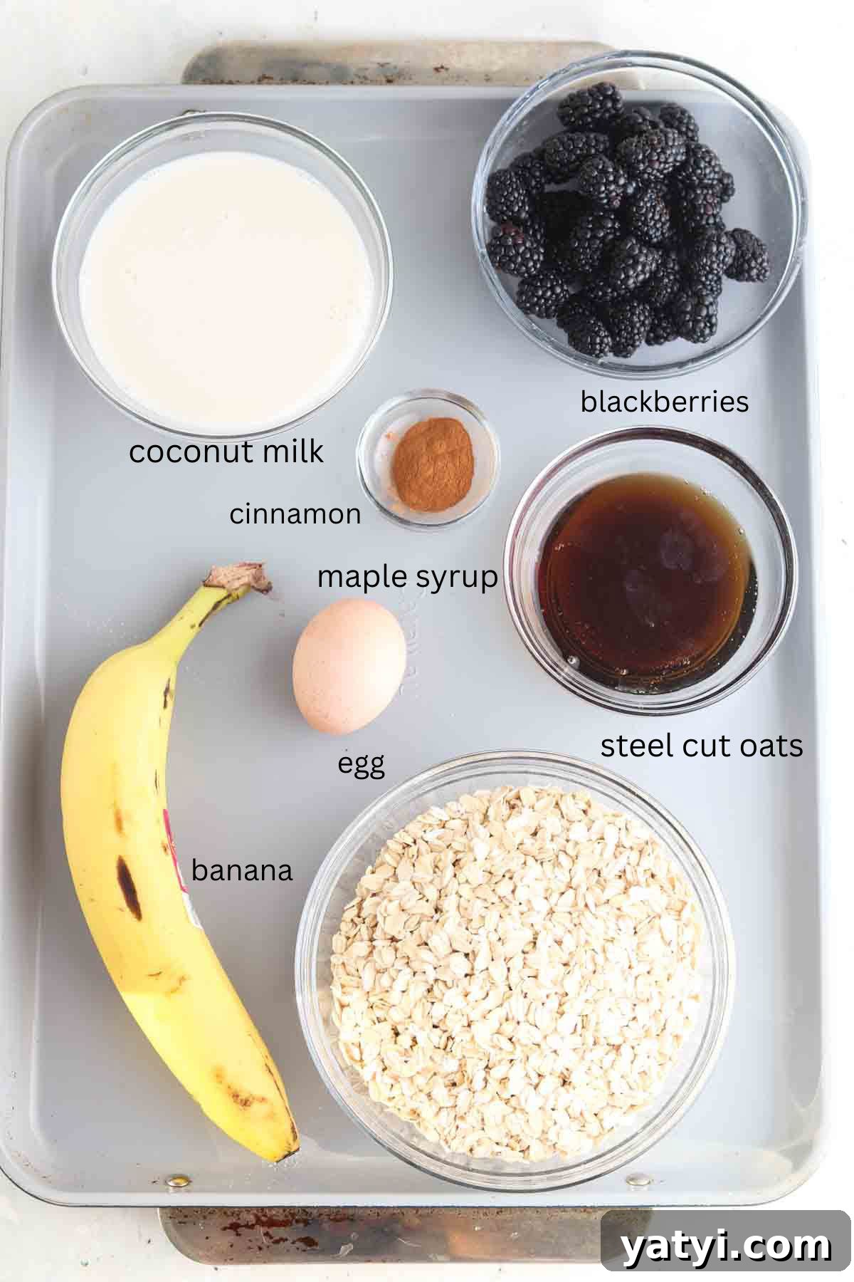 Blackberry Baked Oatmeal Recipe for Summer Brunch 3 Oats, bananas, blackberries, maple syrup, cinnamon, milk and an egg laid out on the counter in glass clear bowls.