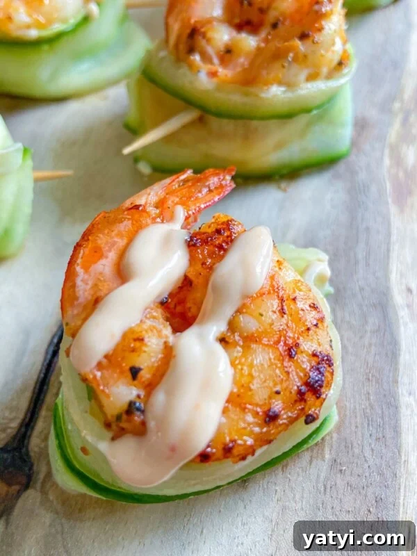 A grilled shrimp topped with creamy sauce rests on a cucumber boat, secured with a toothpick.