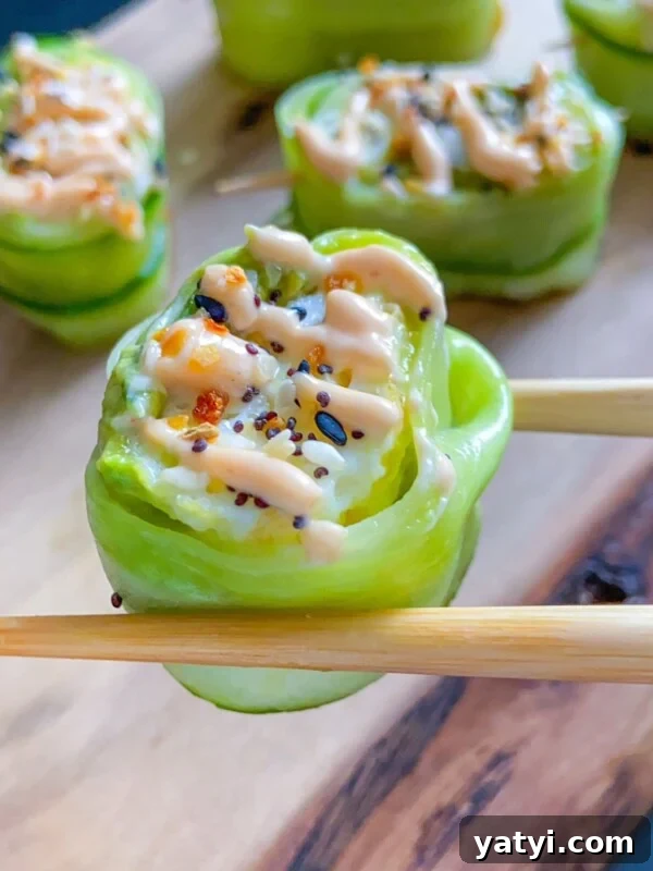 Close-up of chopsticks holding a Shrimp Cucumber Roll wrapped in thin cucumber slices, topped with sauce and sprinkled with sesame seeds.