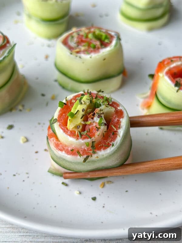 Cucumber and salmon rolls garnished with herbs on a white plate.