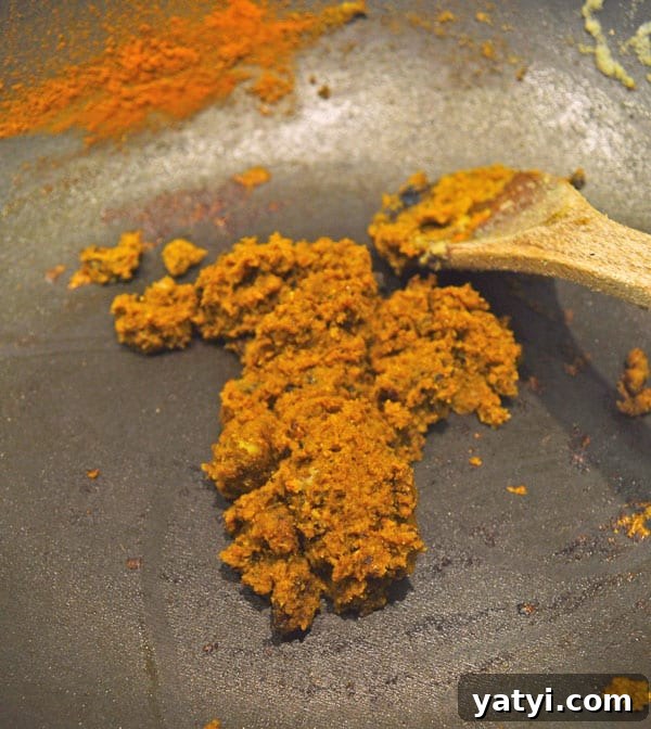 One-Pot Vegan Tikka Masala Recipe for Flavorful Dinner 7 An orange-brown puree with orange spices and a wooden spoon in a black pan.