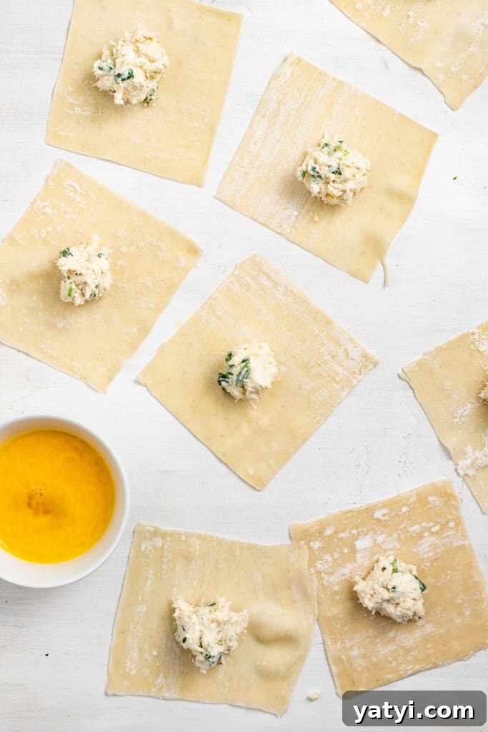Add filling to wrappers. Crab rangoon filling placed in the center of wonton wrappers near a bowl of egg wash.