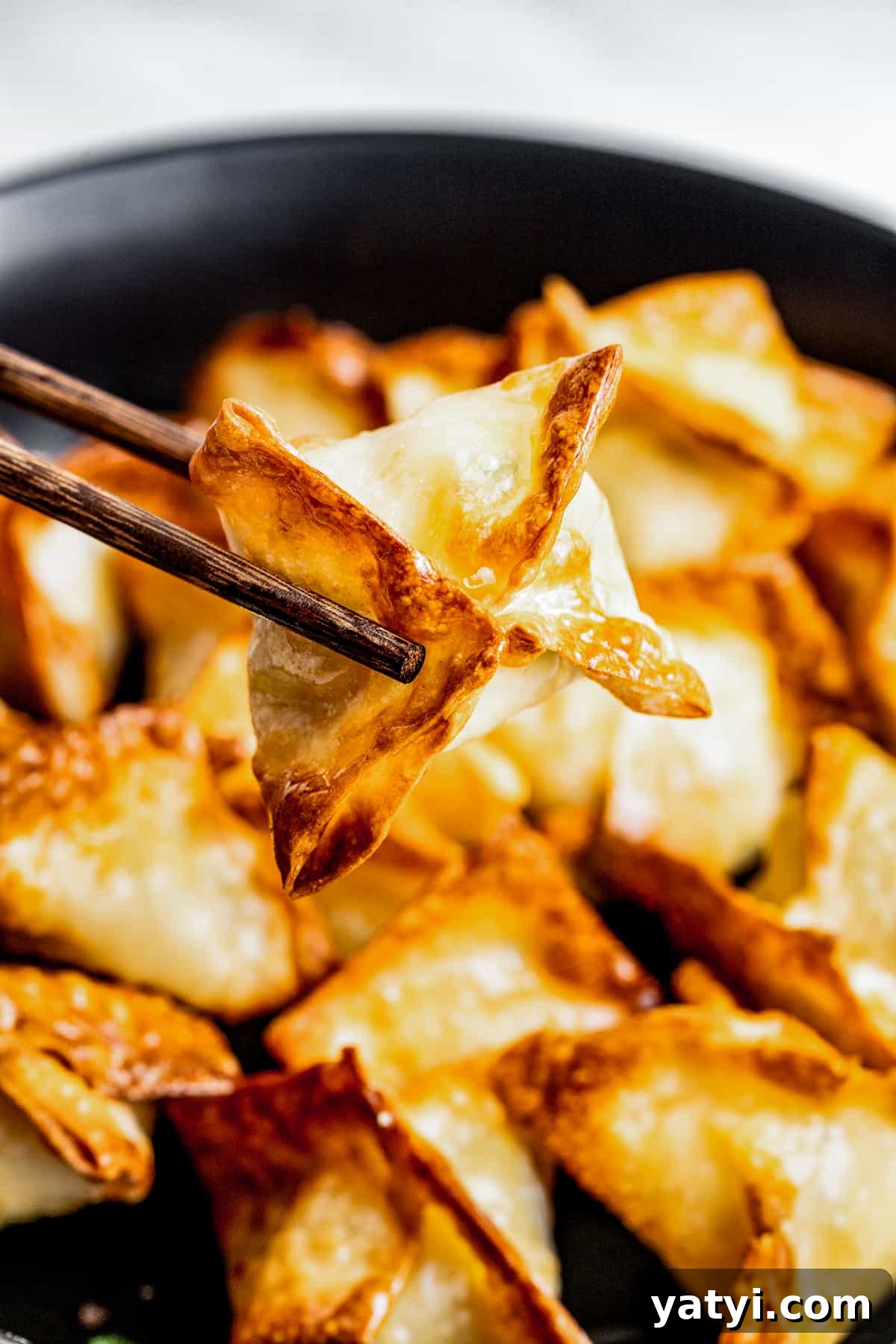Serve with your favorite dipping sauce. Picking up a piece of crab rangoon with chopsticks from a plate.