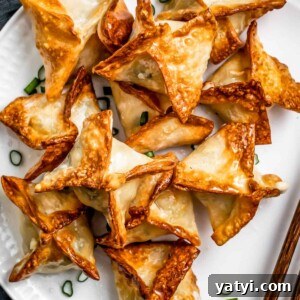 Crispy Air Fryer Crab Rangoon: Quick Seafood Appetizer Recipe 4 Air Fryer Crab rangoon on a white plate garnished with green onions and a pair of chopsticks placed next to the rangoons.