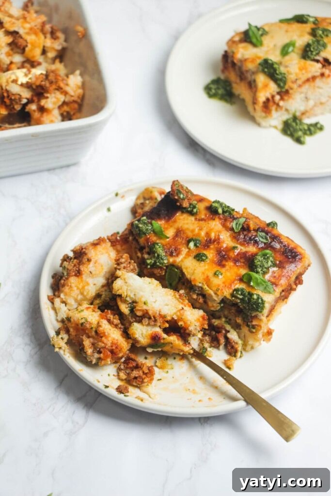 Slice of Bolognese rice bake on a white plate, with another piece on a plate in the background.