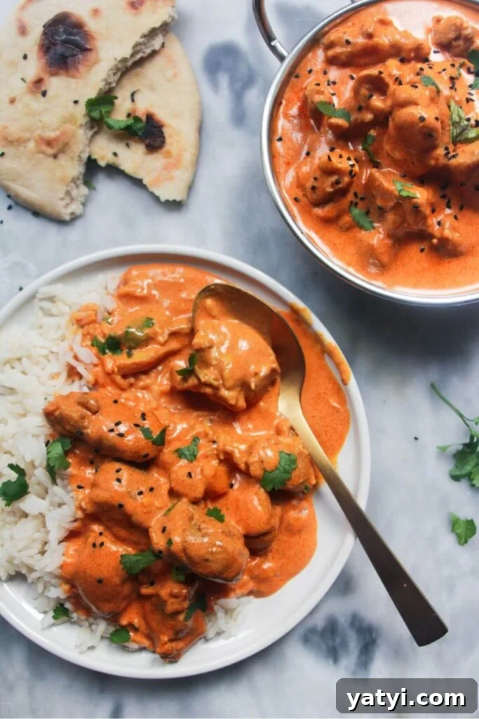 White plate with rice and butter chicken with bowl of butter chicken in the background and garlic naan.