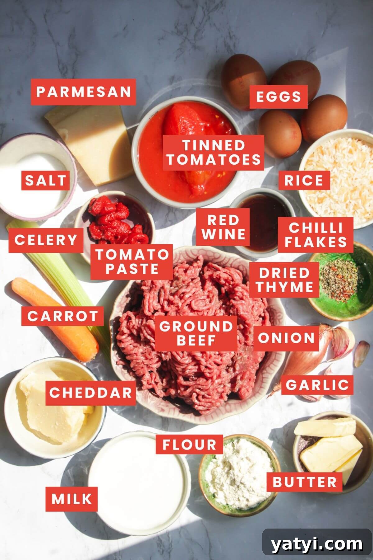 Ingredients for rice bolognese bake laid out on a white marble background and labelled.