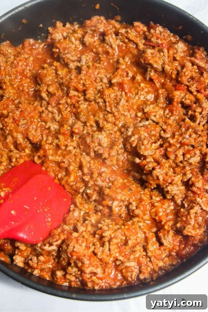 Red spatula stirring cooked bolognese sauce in a pan.