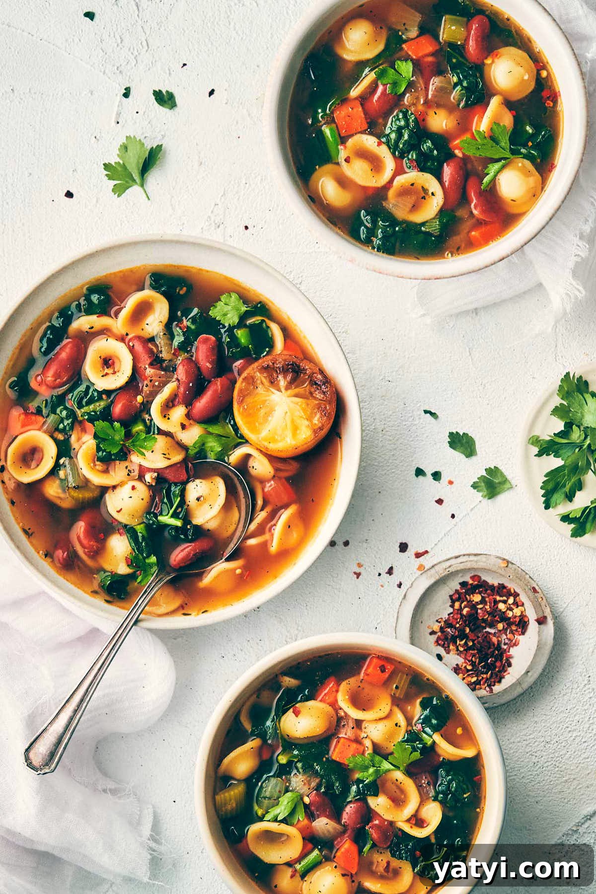Three bowls of veggie bean soup on the counter topped with parsley, pepper and chili flakes