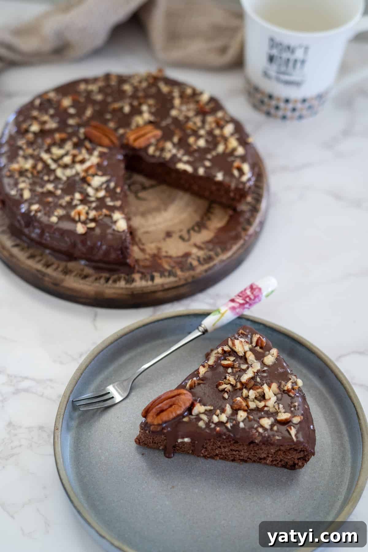 Keto Chocolate Pecan Torte Recipe – Low-Carb Dessert Delight 11 A slice of chocolate pecan torte topped with nuts and a pecan sits on a gray plate next to a fork. The rest of the cake, partially sliced, rests enticingly on a wooden board in the background.