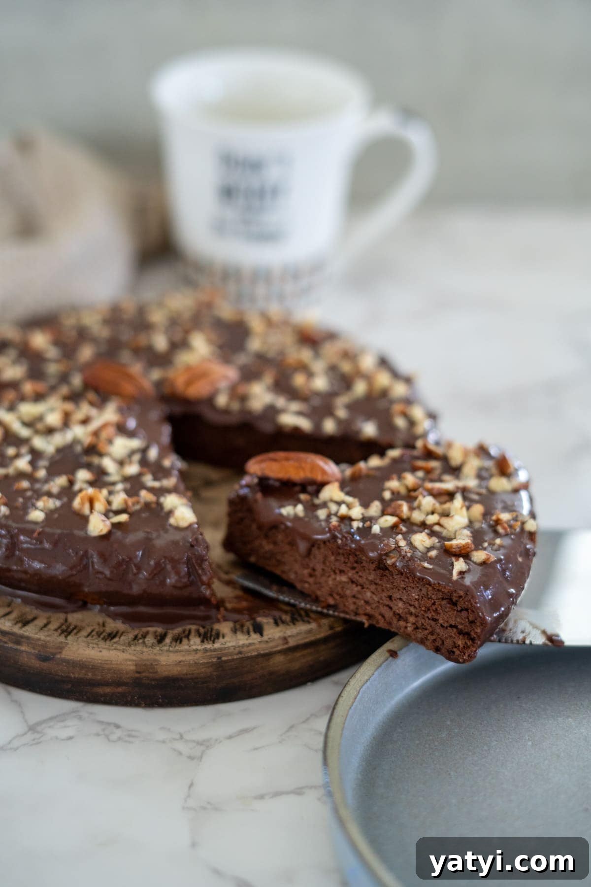 Keto Chocolate Pecan Torte Recipe – Low-Carb Dessert Delight 3 A pecan torte topped with chopped nuts and one slice resting on a metal spatula. A mug is blurred in the background.