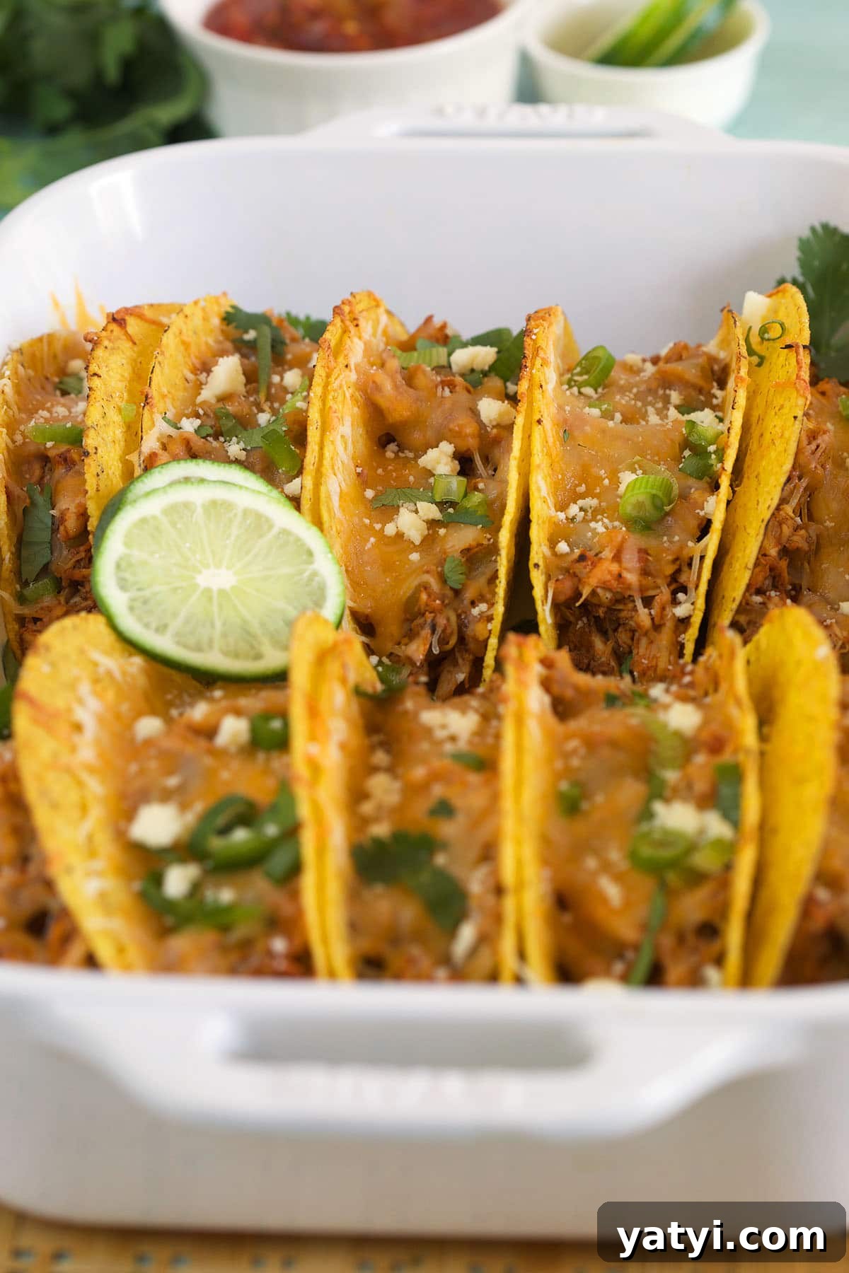 Oven-Baked Chicken Tacos with Crispy Seasoned Filling 3 Sliced limes are placed on top of baked tacos in a white dish.