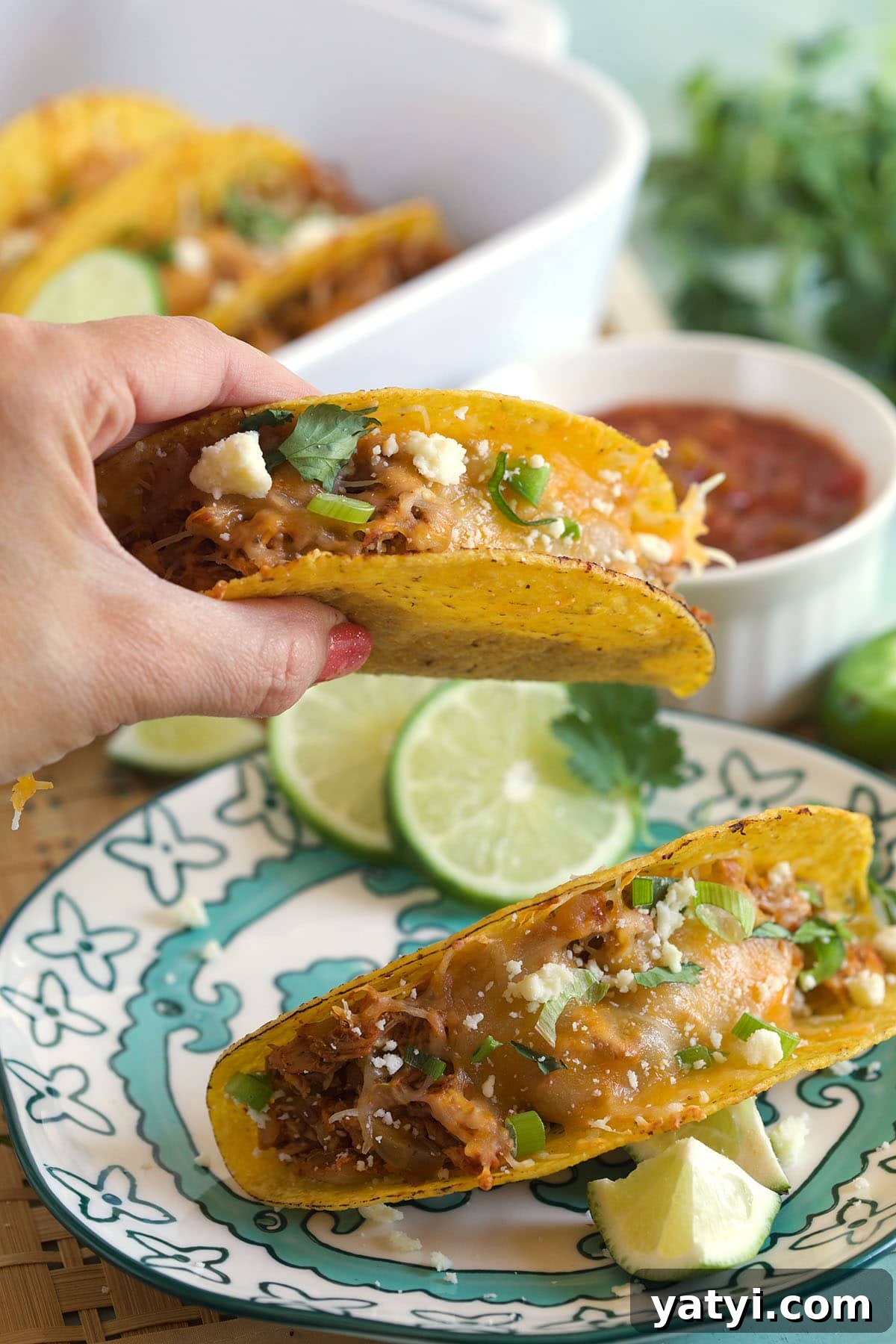 Oven-Baked Chicken Tacos with Crispy Seasoned Filling 5 A taco is being lifted from a plate.