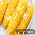 Four ears of smoked corn on the cob on a plate with butter on top.