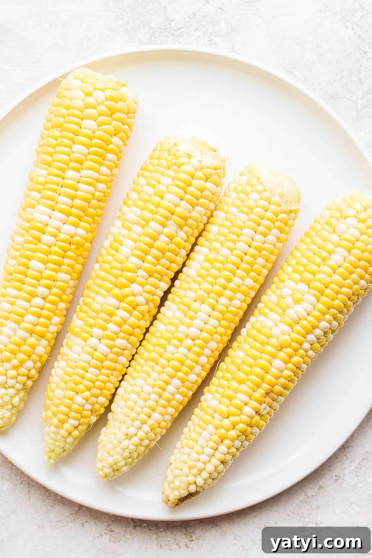 Ultimate Smoked Corn on the Cob Recipe for Sweet, Smoky Flavor 3 Four ears of shucked corn on a white plate.