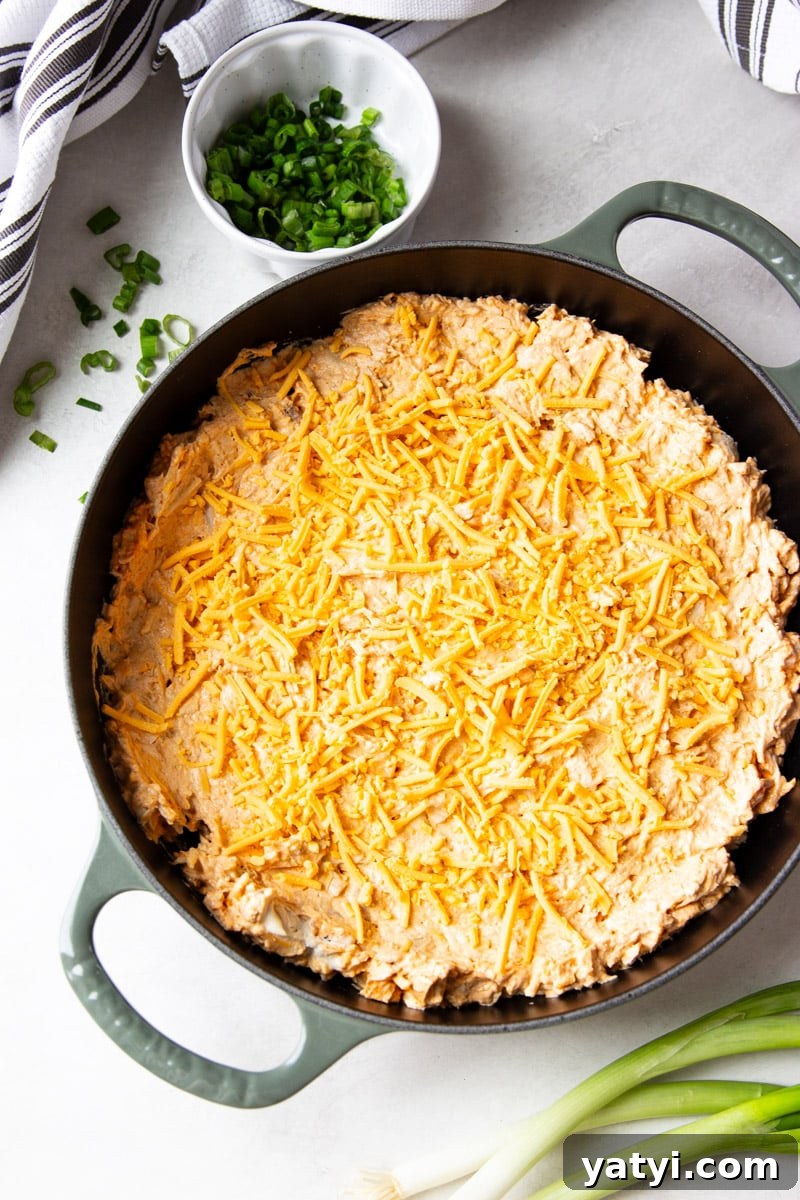 Creamy Buffalo Chicken Dip Recipe for Game Day or Parties 6 Green onions in a white bowl, white and black dish towel, unbaked buffalo chicken dip in a skillet.
