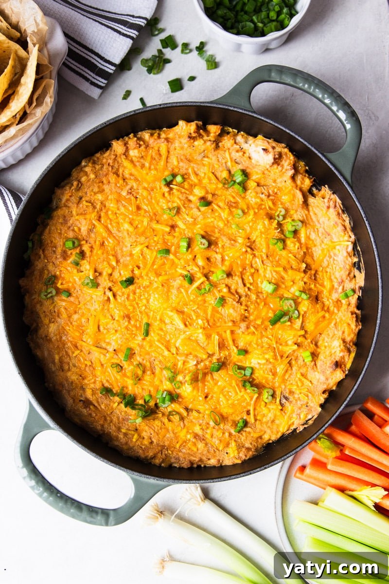 Creamy Buffalo Chicken Dip Recipe for Game Day or Parties 7 Baked buffalo chicken dip in a skillet, green onions, white dish towel, corn chips, celery, and carrots.