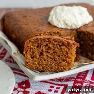 Gingerbread snack cake sliced on a platter with a dollop of whipped cream in the background.