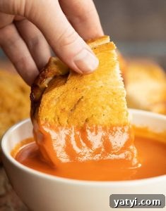 Air Fryer Grilled Cheese close up shot of hand dunking grilled cheese into small white bowl of tomato soup