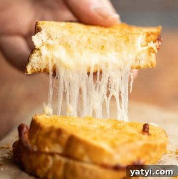 close up shot of hand pulling up half of grilled cheese with cheese dripping out