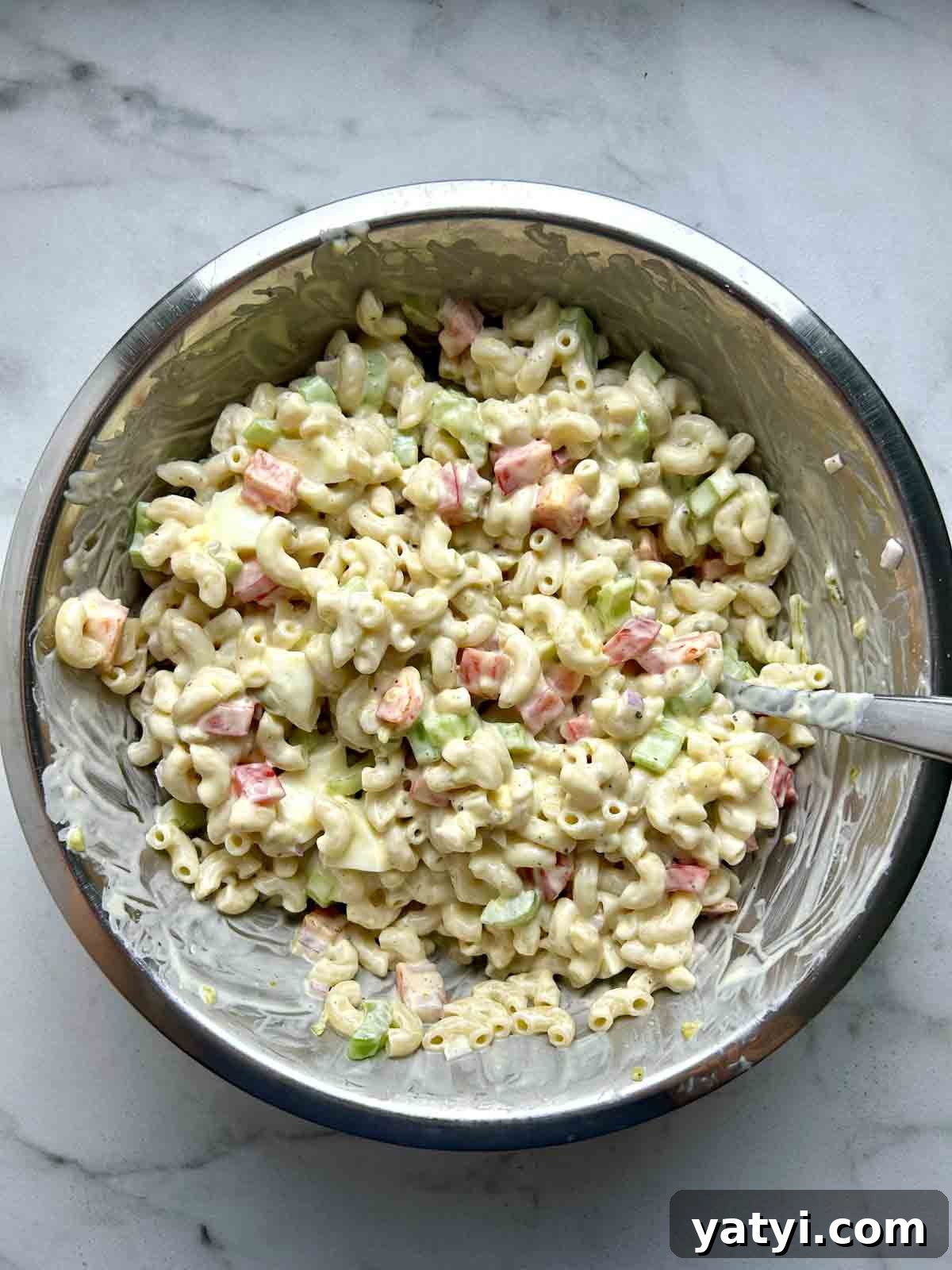 Creamy Classic Macaroni Salad Recipe for Picnics and Potlucks 6 dressing mixed with macaroni and vegetables in metal bowl.