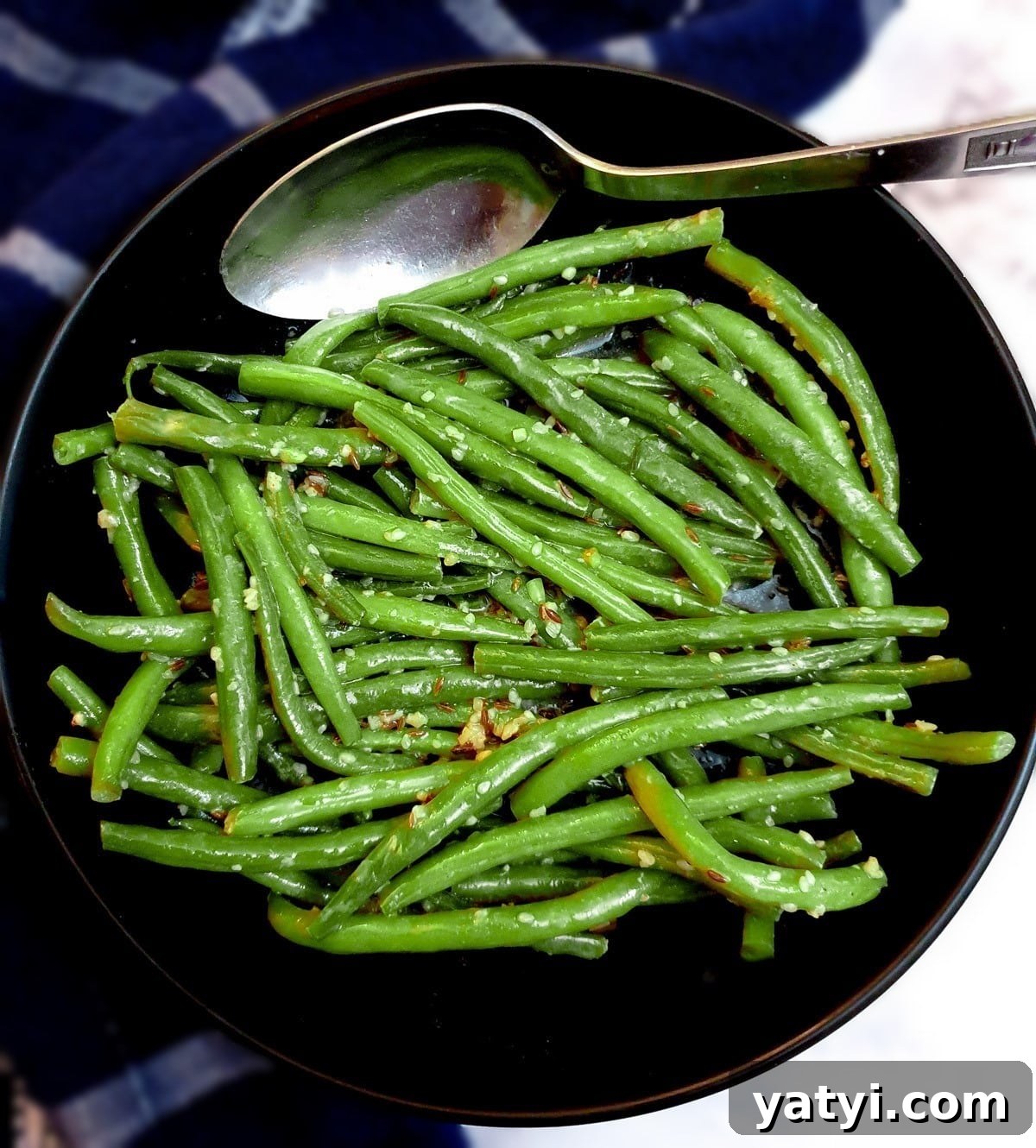 A black serving dish of Indian-style green beans with a serving spoon.