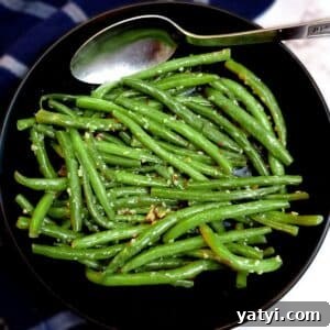 A black serving dish of Indian-style green beans with a serving spoon.