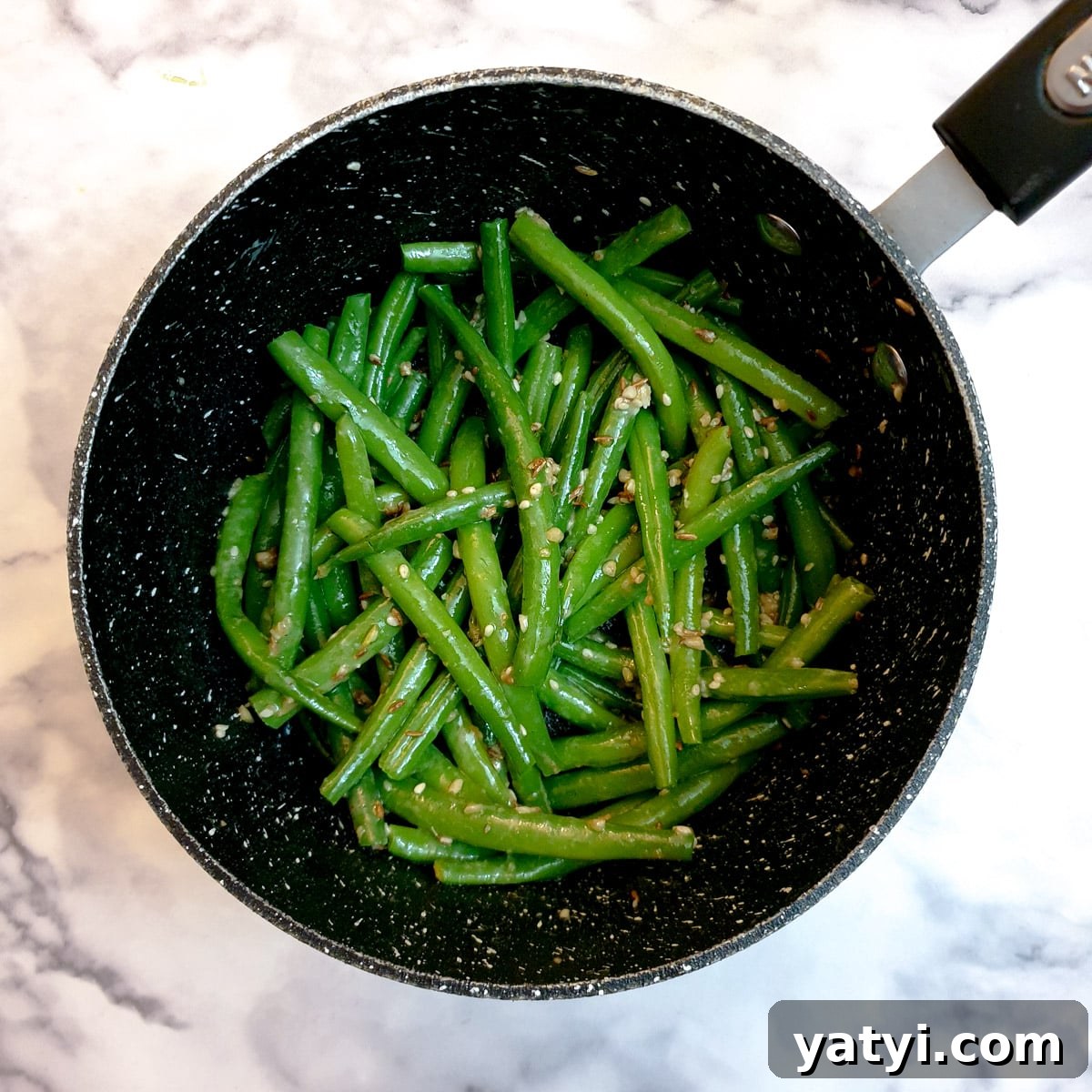 Indian-style green beans in a saucepan, mixed with the fried spices.