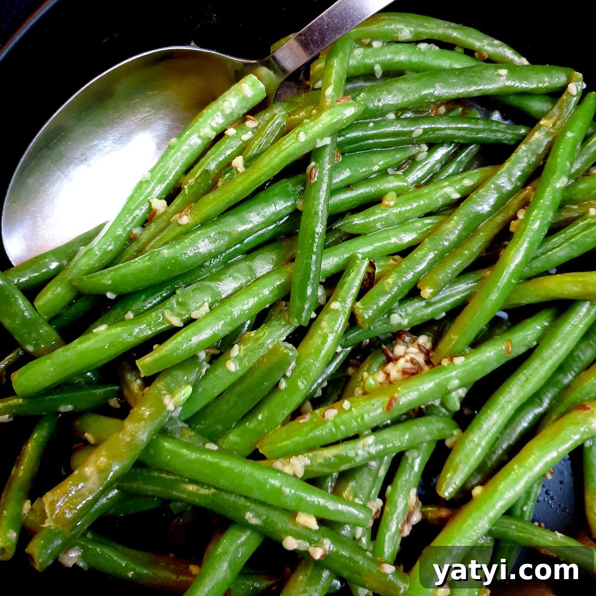 Close up of Indian-style green beans in a black dish with a serving spoon.