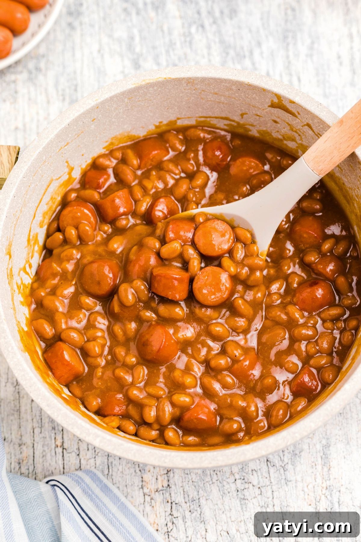Classic Beanie Weenies Recipe: Hearty Sausage and Beans Meal 2 Juicy Beanie weenies being scooped up out of a large saucepan.