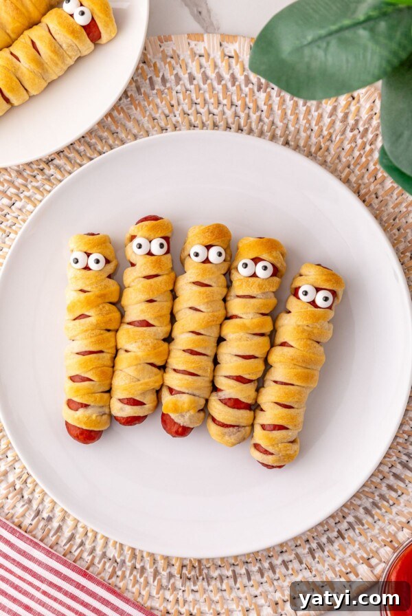 Classic Beanie Weenies Recipe: Hearty Sausage and Beans Meal 12 Mummy hot dogs on a white plate, with candy eyes.