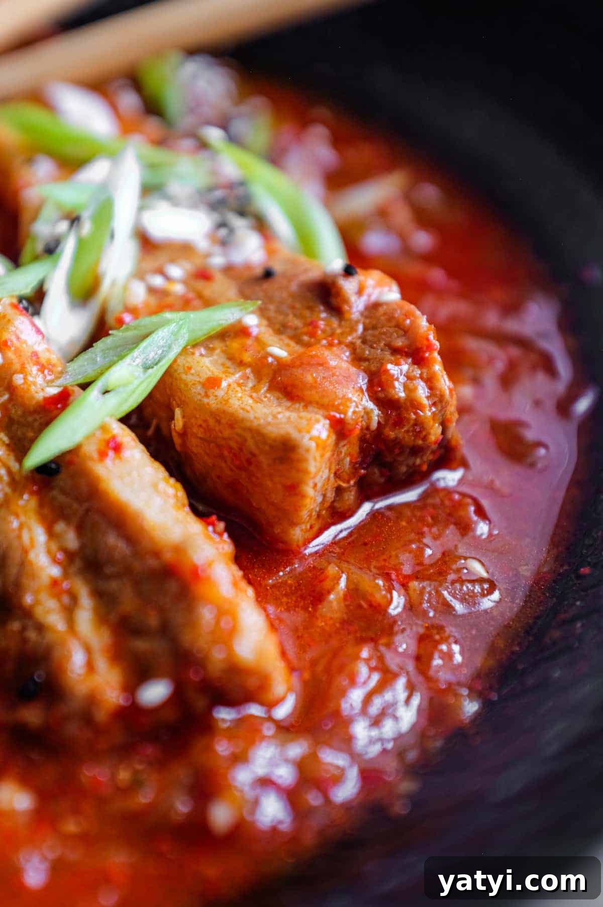 Kimchi Pork Stew | cookeatworld.com A large black bowl of Kimchi Pork Stew scattered with sesame seeds, nigella seeds and spring onion