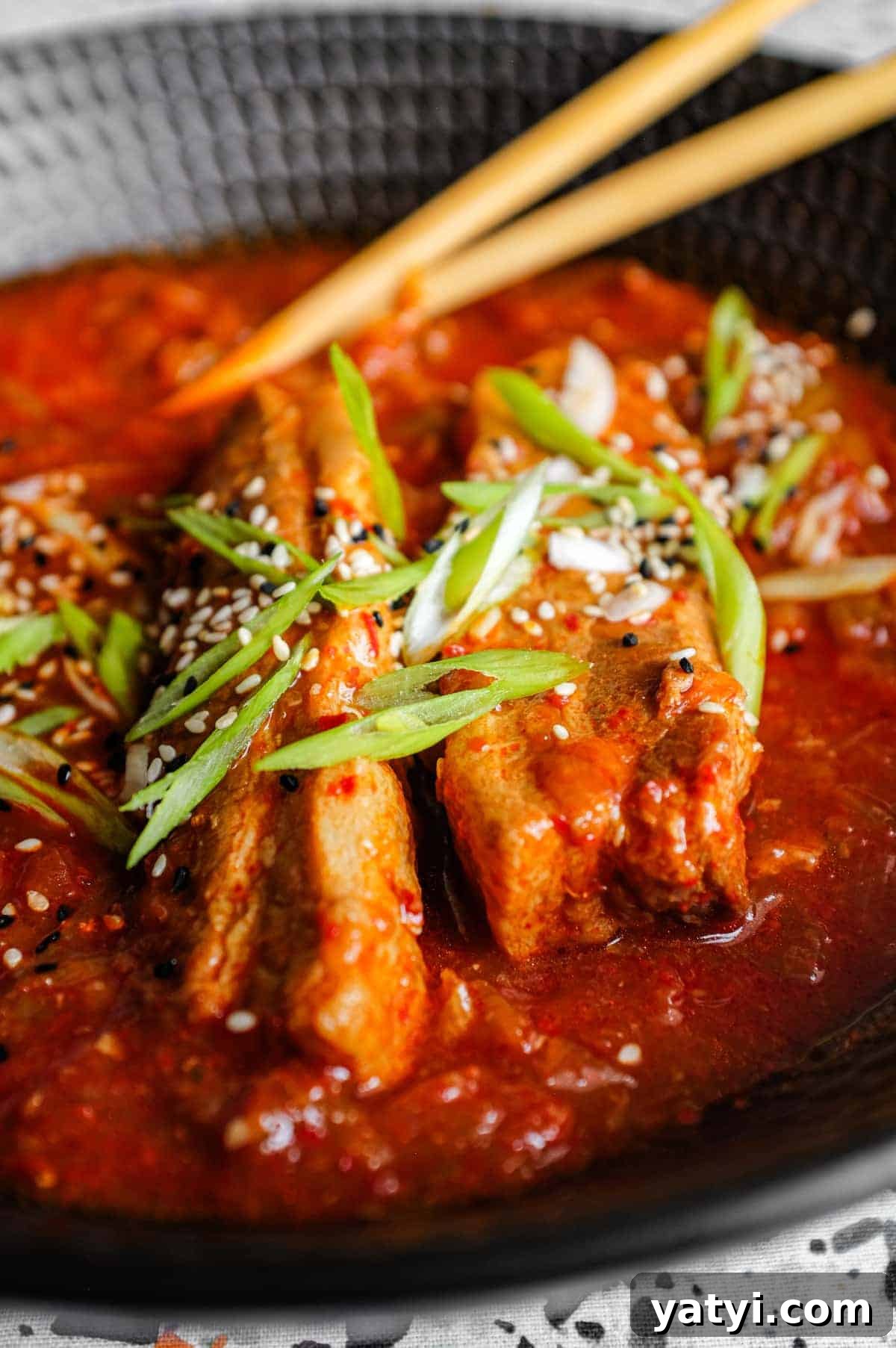 Kimchi Pork Stew | cookeatworld.com A large black bowl of Kimchi Pork Stew scattered with sesame seeds, nigella seeds and spring onion with chopsticks on the side.