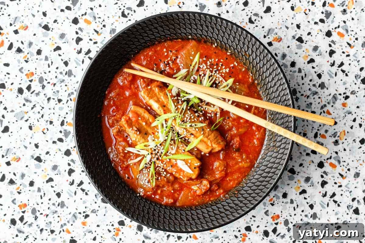 Spicy Kimchi Pork Stew Recipe for Savory Comfort Meals 2 A large black bowl of Kimchi Pork Stew scattered with sesame seeds, nigella seeds and spring onion with chopsticks on the side.
