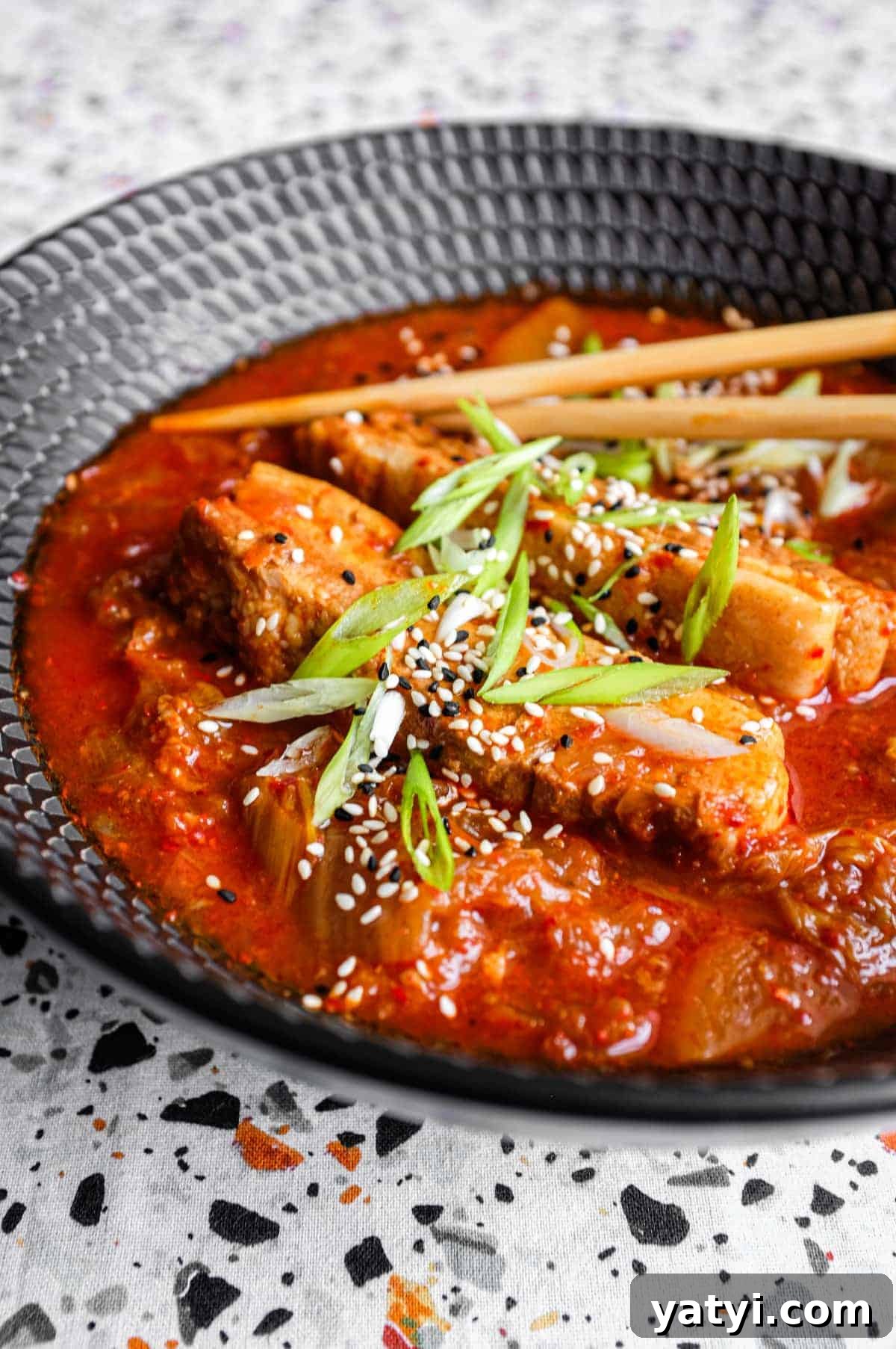 Kimchi Pork Stew | cookeatworld.com A large black bowl of Kimchi Pork Stew scattered with sesame seeds, nigella seeds and spring onion with chopsticks on the side.